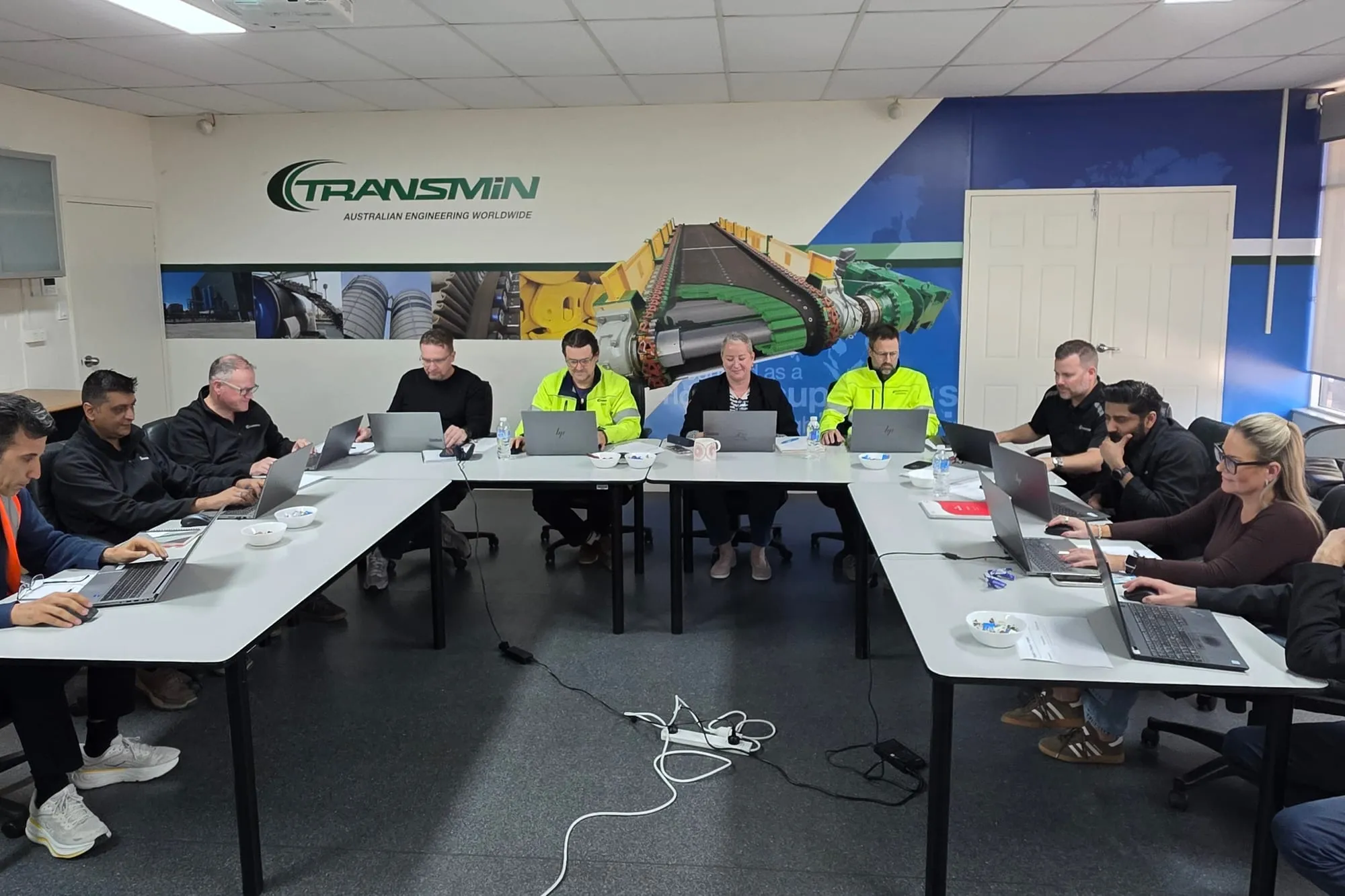 The Transmin leadership team working at their laptops around a U-shaped table during an AI session
